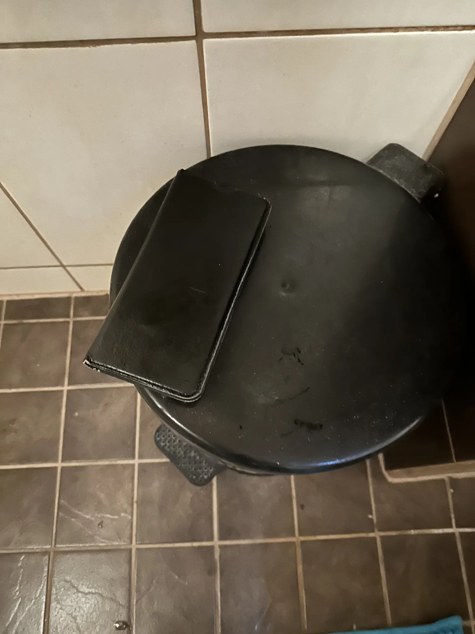 kuvassa musta suojakuorellinen puhelin roska-astian kannen päällä